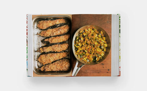 Book open to a page with images of fried food and a dish of vegetables on a wooden board.