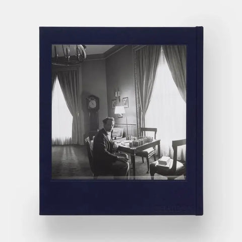 Framed black and white photograph of a man in a room with curtains and a desk.