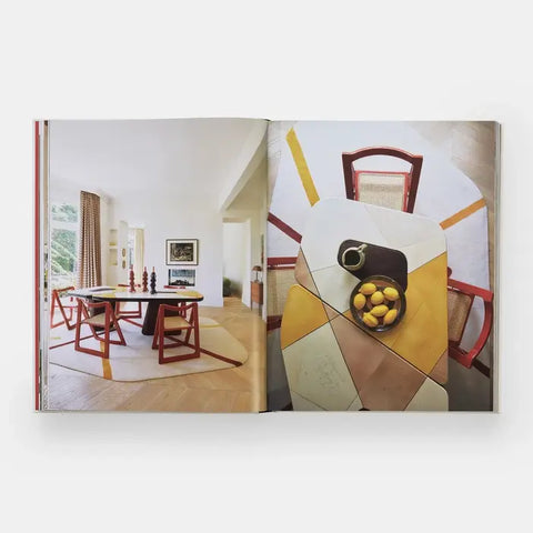 Book open to a page showing a dining room with red chairs and a geometric abstract painting.