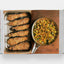 Book open to a page with images of fried food and a dish of vegetables on a wooden board.