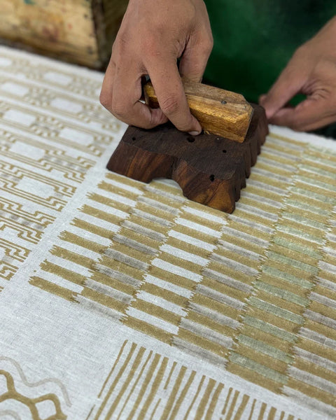 A close-up of a person's hands hand blocking a patterned textile. 