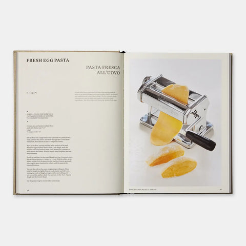 Open book showing a pasta maker with fresh egg pasta on a white background